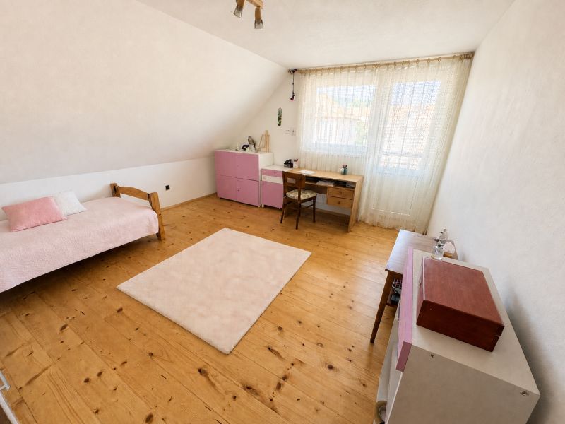 A room in a family house with wooden decor, pink furniture, and a writing desk.