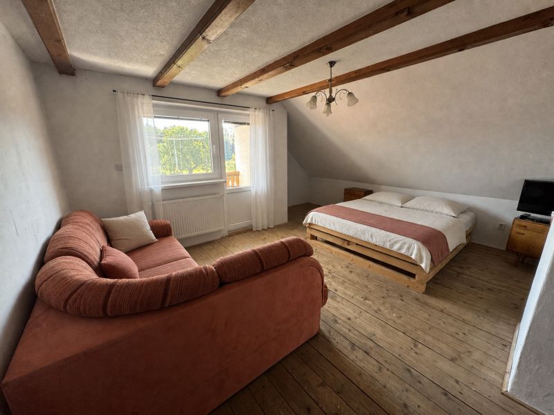 A bedroom in a family house with a wooden decor floor, a sofa, and a bed.