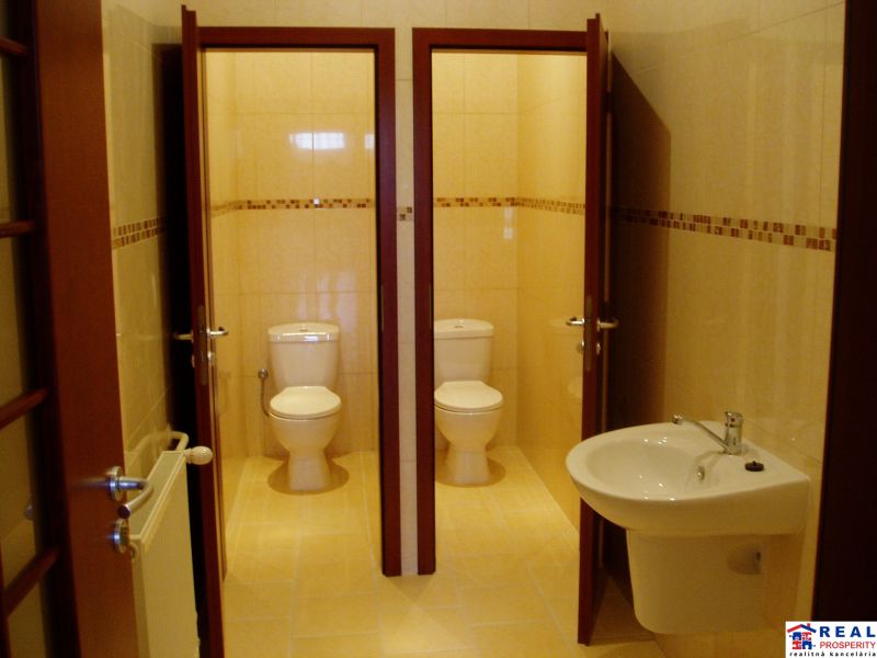 Interior of offices with two toilets and a sink on light tiles.