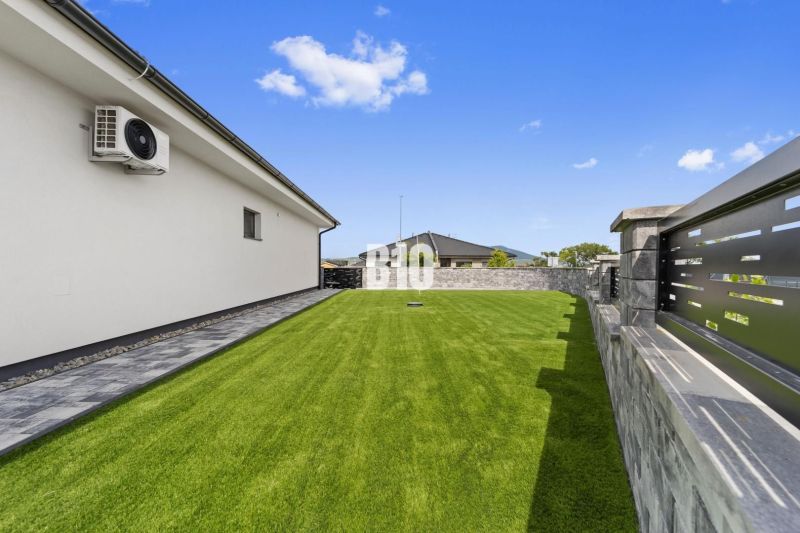 The garden of a family house in Nitra with a lawn and stone paving by the wall.
