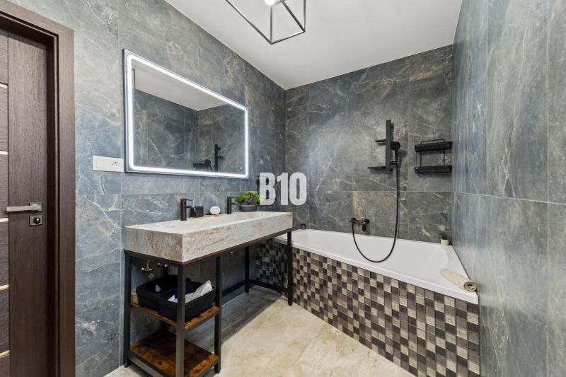 A bathroom in a family house with a bathtub, stone tiles, and a large mirror.