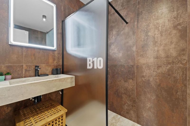 Bathroom with a translucent shower wall, stone sink, and decorative lighting.