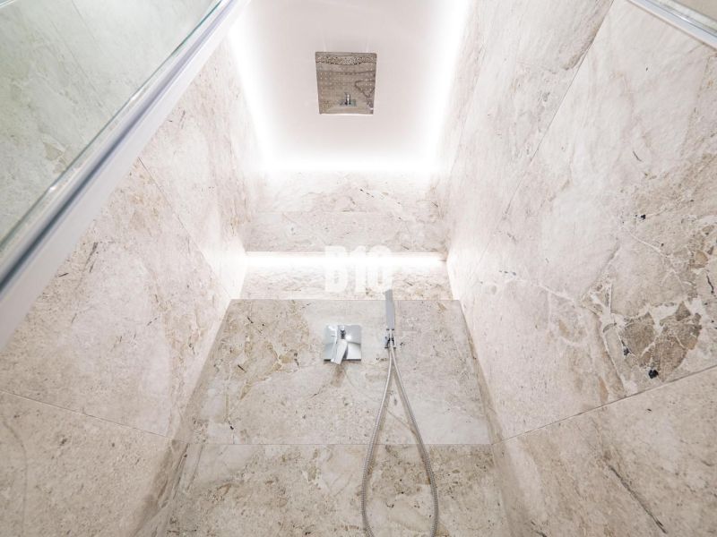 Shower enclosure with light stone tiles in a 3-room apartment.