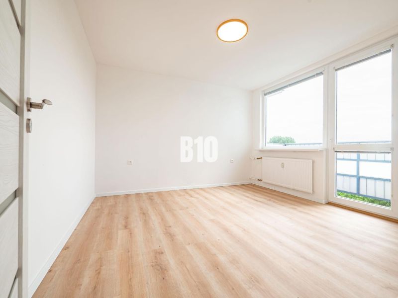 A room in a 3-room apartment with a wooden decor floor and large windows.