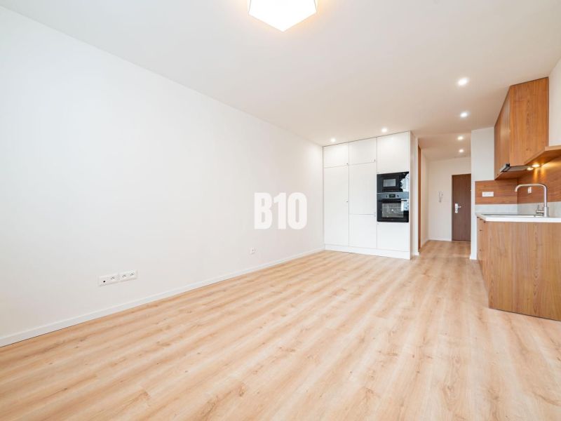 A bright kitchen with white cabinets and a wood-patterned floor in a three-room apartment.