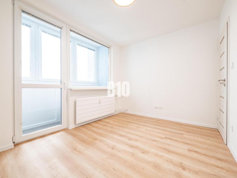A spacious room in a 3-room apartment with large windows and a wooden decor floor.