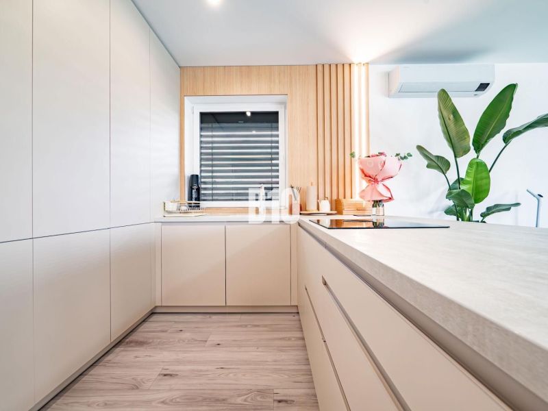 A kitchen in a family house with a wooden decor floor, white cabinets, and flowers.
