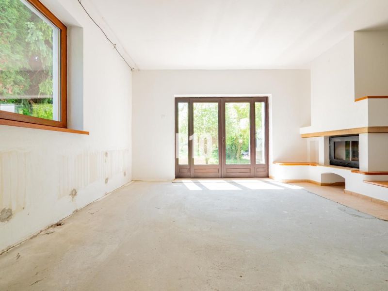 Living room in a family house with spacious windows and a fireplace, without floor covering.