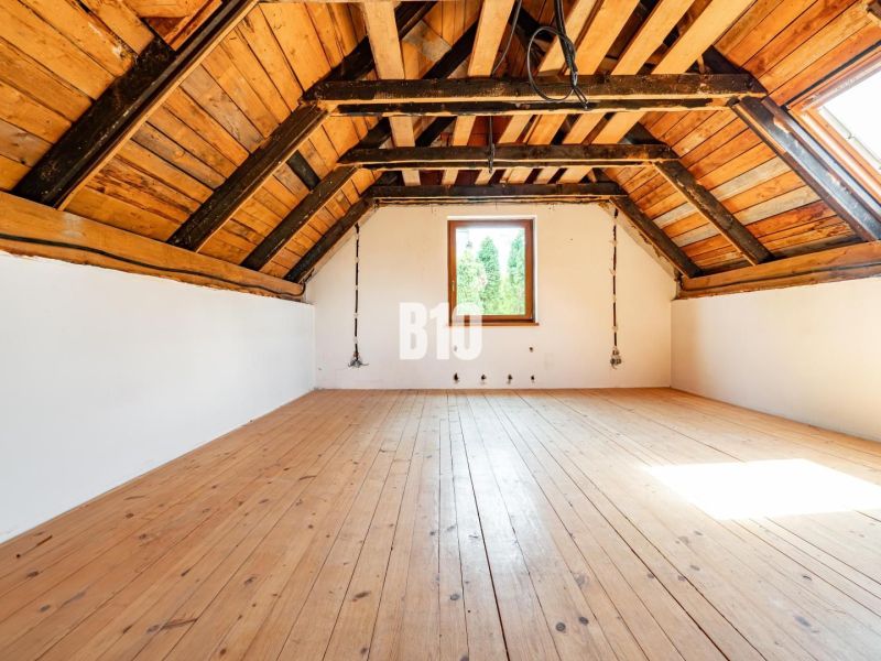 Attic room with wood-decor flooring in a family house, illuminated by a large window.