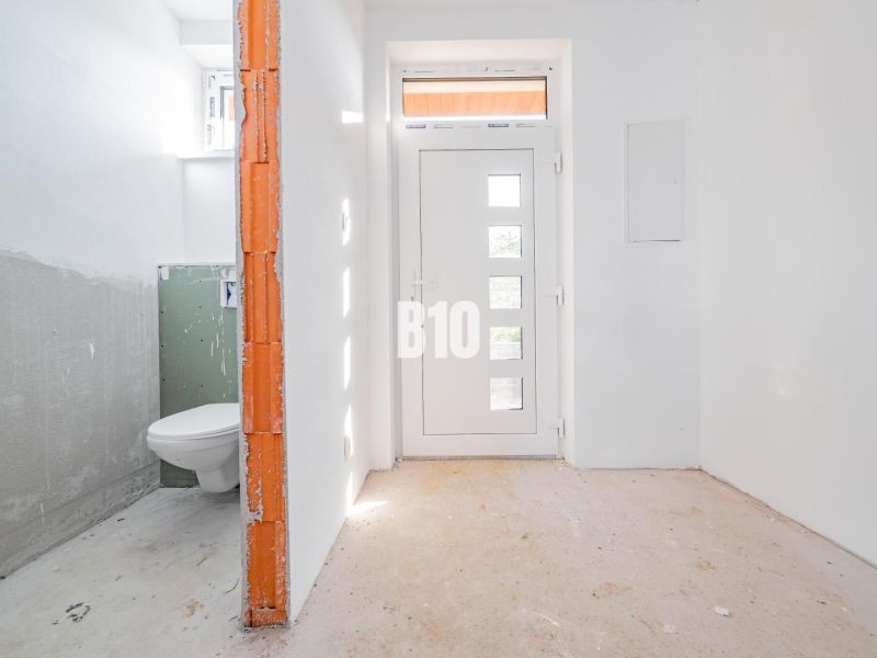 White hallway of a family house with entrance doors and a bathroom on the left.