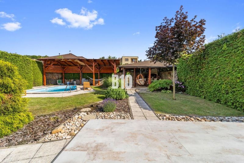 A garden of a family house in Nitra with a swimming pool and a gazebo surrounded by greenery.