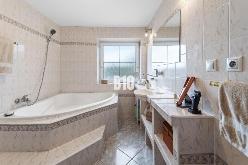 A bathroom in a family house with a corner bathtub and a window, light tiles.