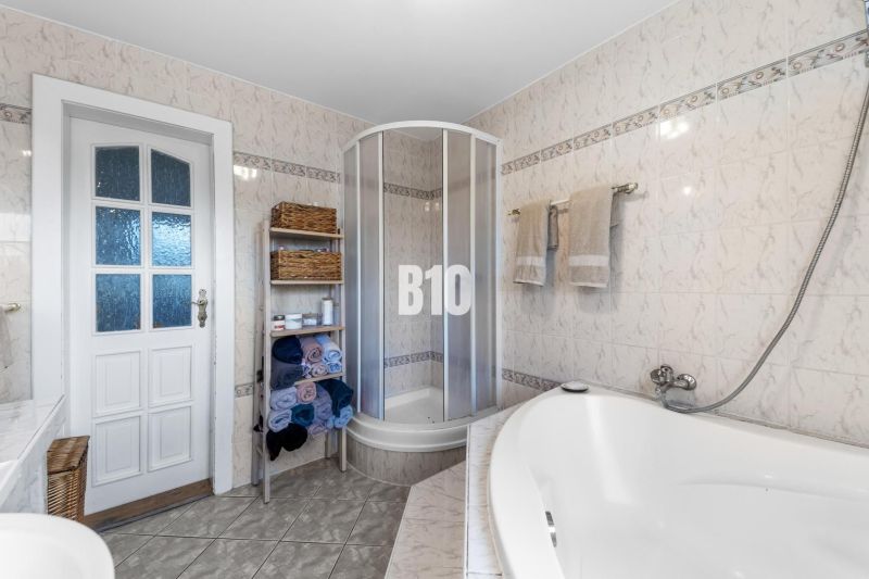 A bathroom in a family house with a bathtub, shower, and a towel shelf.