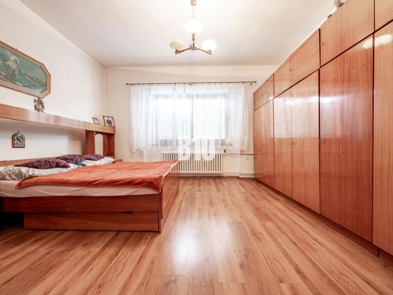 Bedroom in a family house with a bed, wardrobe, and wooden decor flooring.