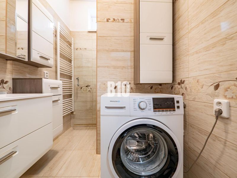 A bathroom in a family house with a washing machine and light-colored tiles.