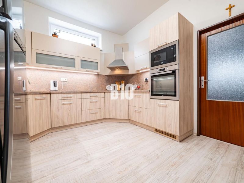 A kitchen in light tones with a wood-patterned floor and built-in appliances.