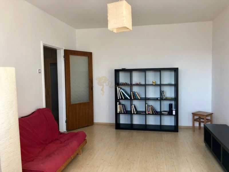 A room in a one-room apartment with a shelving system, a red sofa, and a wooden decor floor.