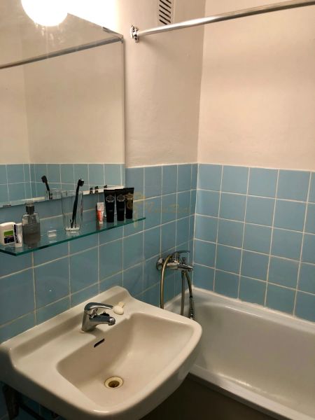 A bathroom with blue tiles, a sink, a bathtub, and a mirror in a studio apartment.