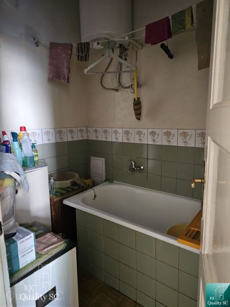 A bathroom in a 2-room apartment with a bathtub, tiles, and a clothes rack.