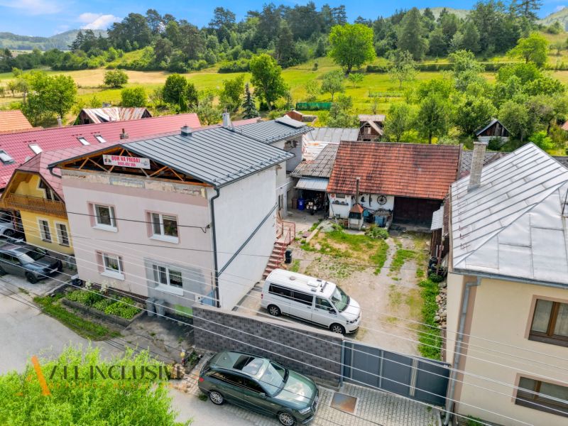 A family house in Dúbravica surrounded by greenery with parking and neighboring buildings.