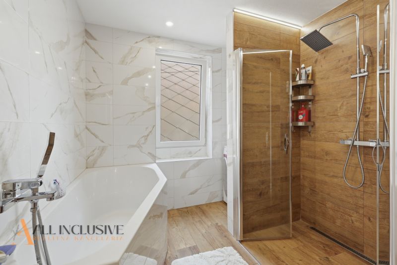 A bathroom in a family house with a bathtub, a shower corner, and a floor with a wooden decor.