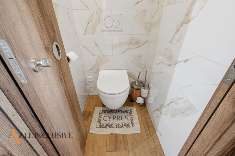 A toilet in a family house with a wooden decor floor and ceramic tiles.