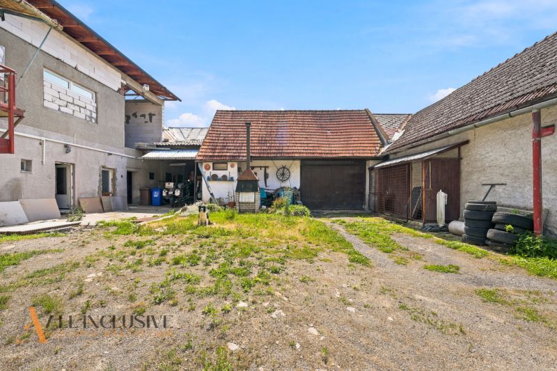 The courtyard of a family house in Dúbravica with farm buildings and a dog on the property.