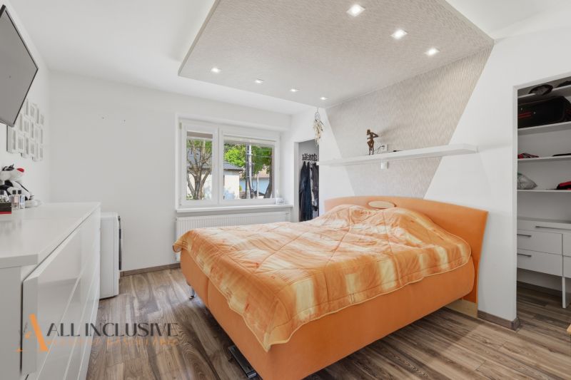 A bedroom with an orange bed, white furniture, and a wood-patterned floor in a family house.