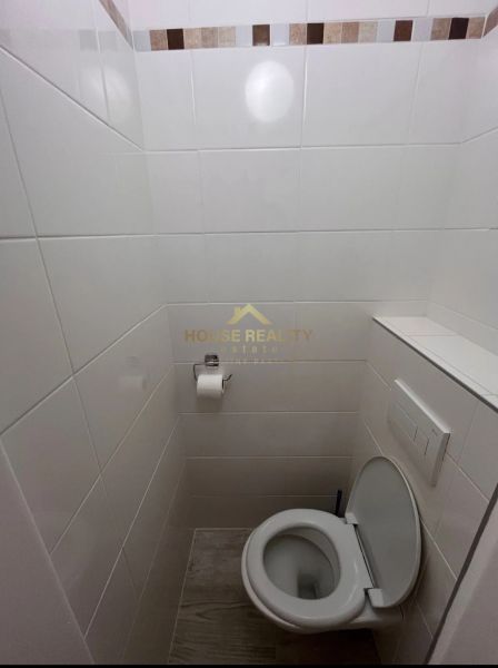 A toilet with white tiles and mosaic decor in a studio apartment.