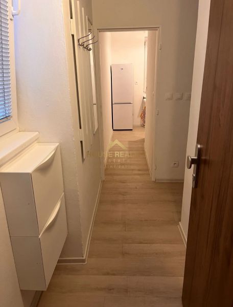 A hallway with a wooden decor floor leads to a white refrigerator in a studio apartment.