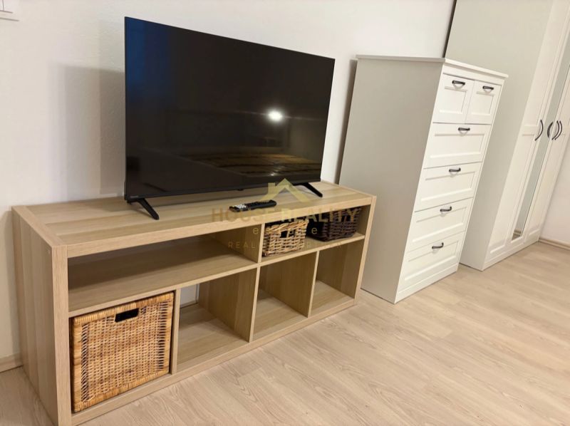TV on a shelf with baskets, next to a dresser and a wardrobe, floor with wooden decor.