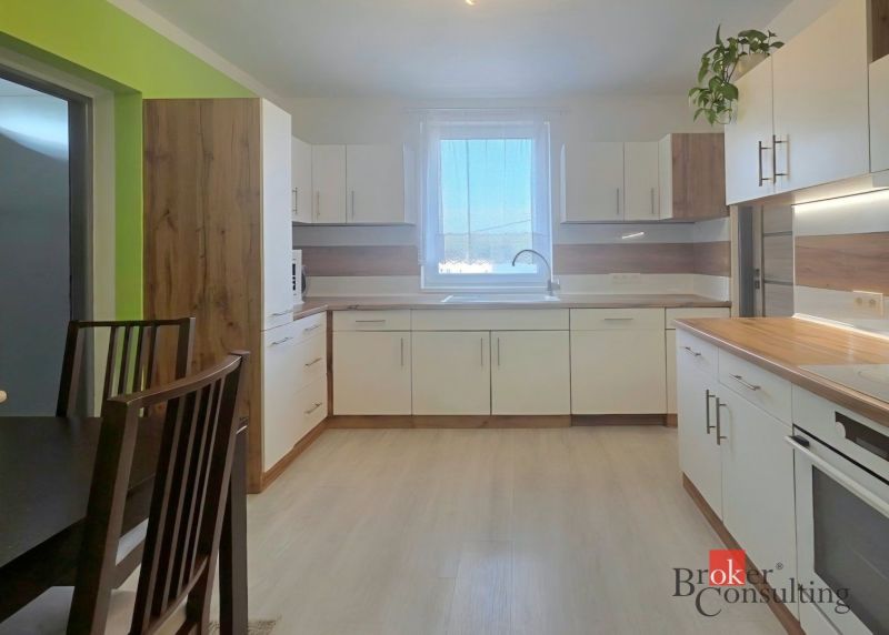 Kitchen in a 4-room apartment with white cabinets and wooden decor on the floor.