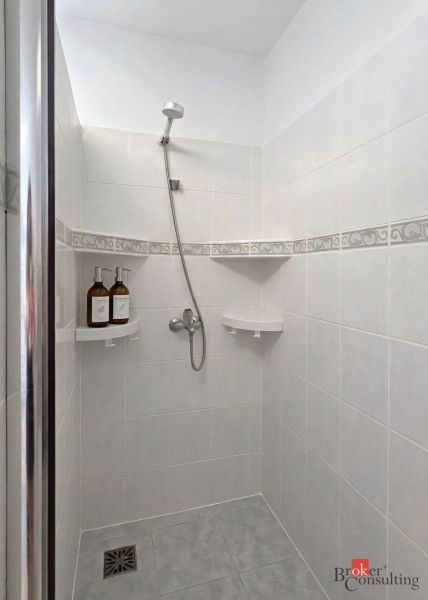 A shower corner in a 4-room apartment with light tiles and corner shelves.