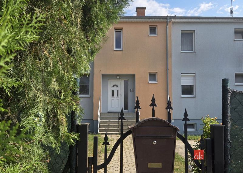 Entrance to a terraced house with a gate, trees, and a mailbox in Blatná na Ostrove.