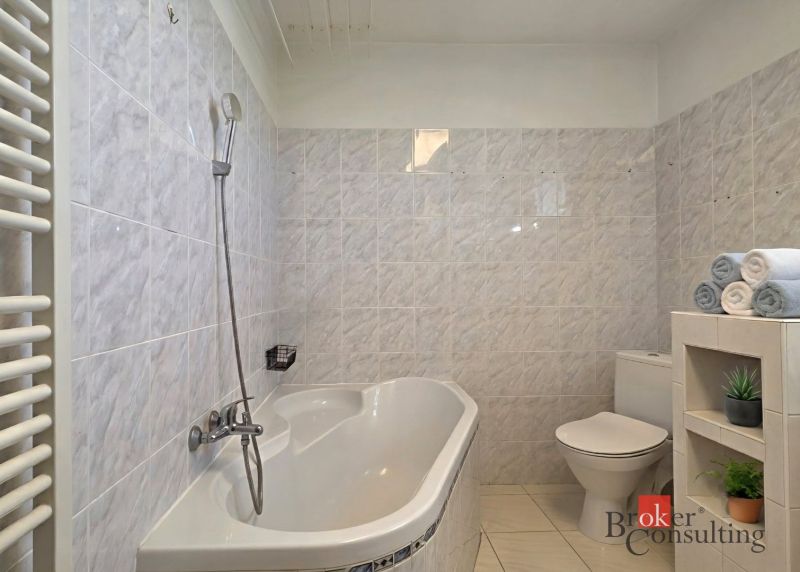 A bathroom in a 4-room apartment with a bathtub, toilet, and a shelf with towels.