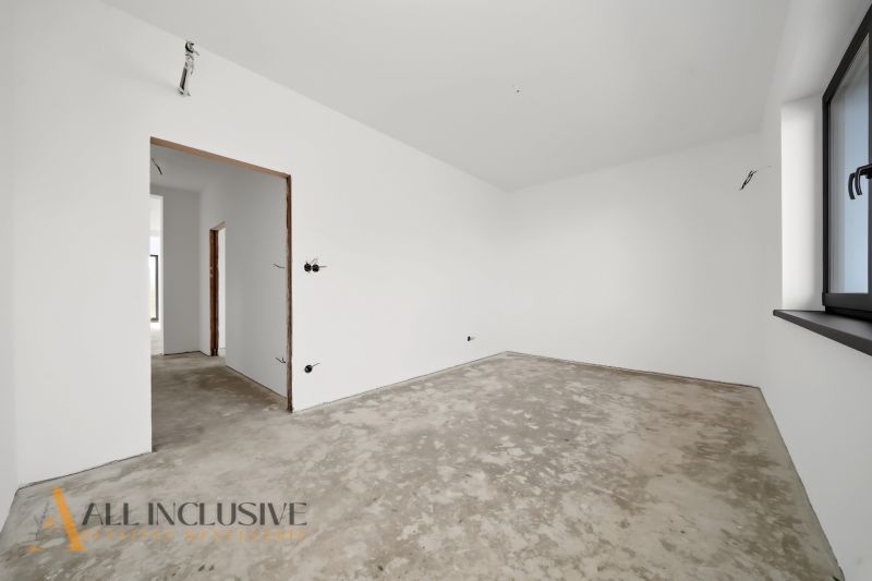 An unfurnished room with white walls and a raw floor in a family house.