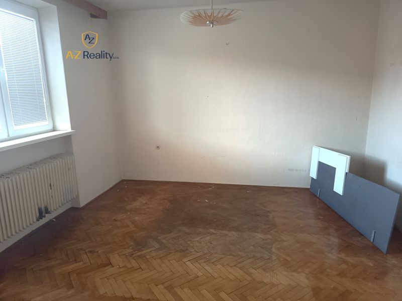 An empty room with a radiator and a wooden-patterned floor in a family house.