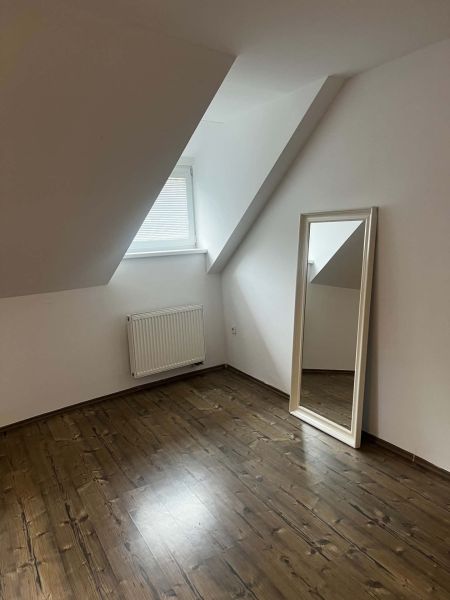 Attic room with wooden decor flooring and a large mirror in a 2-room apartment.