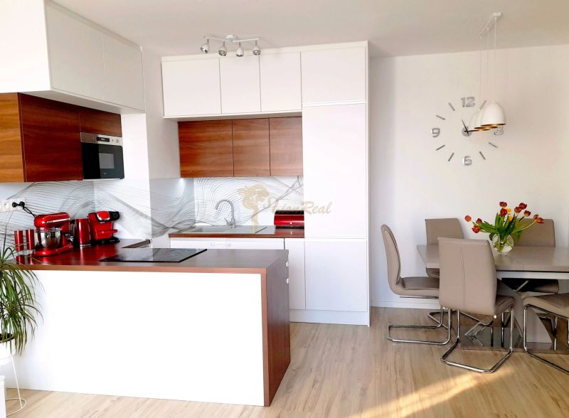 A kitchen with an island, white and wooden cabinets in a 3-room apartment with a wooden decor floor.