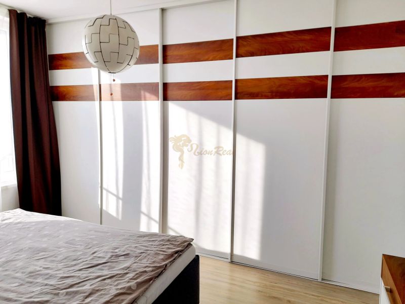 A bedroom in a three-room apartment with a wooden decor floor and a built-in wardrobe.