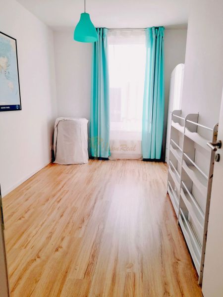 A room in a 3-room apartment with a wood-patterned floor and turquoise curtains.