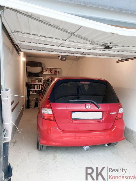 A red car parked in a garage with shelves on the wall, tiled floor.