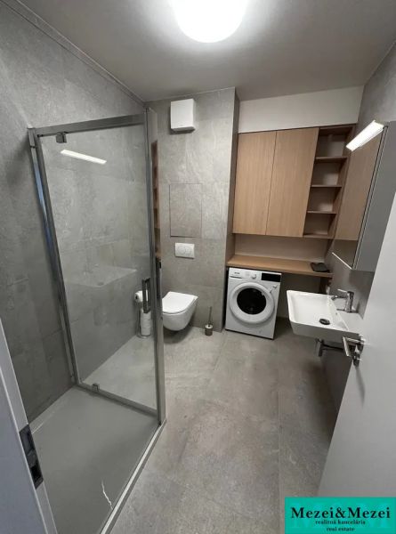 A bathroom in a studio apartment with an elegant shower and a washing machine next to the sink.