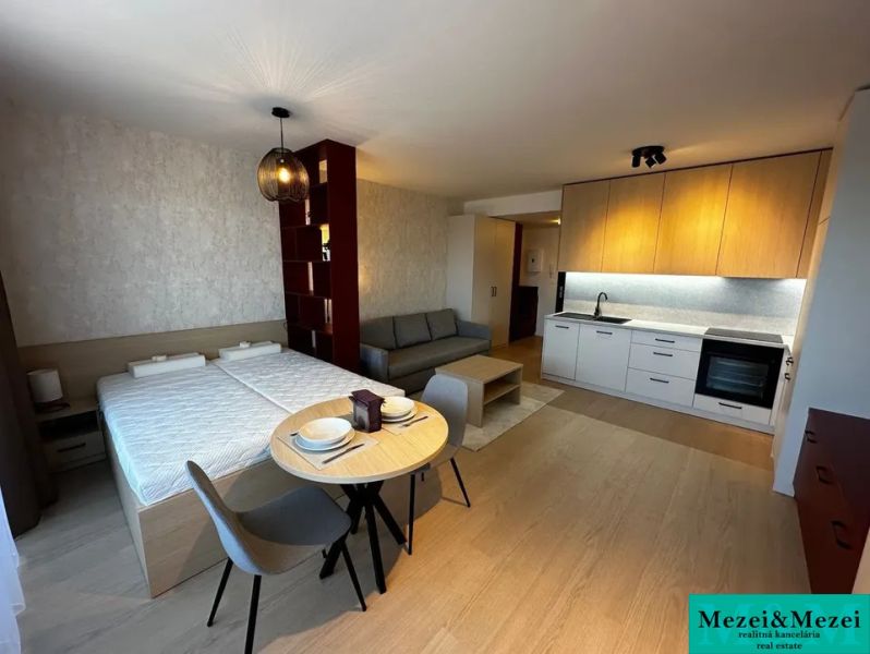 Interior of a 1-room apartment with a kitchenette, bed, and table on a floor with a wooden decor.