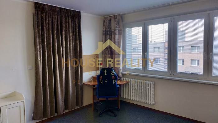 A desk by the window in a studio apartment with curtains and a view.