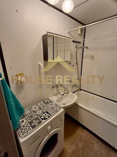 A bathroom in a studio apartment with a washing machine and a bathtub, light walls, and a mirror.