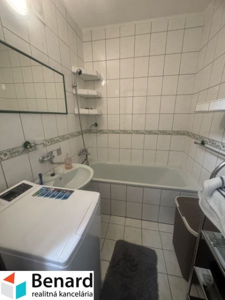 A bathroom in a 2-room apartment with a bathtub, sink, and washing machine, tiled with white tiles.