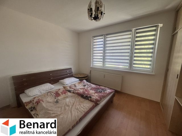 Bedroom in a 2-room apartment with a bed, next to a window with blinds and a wardrobe.