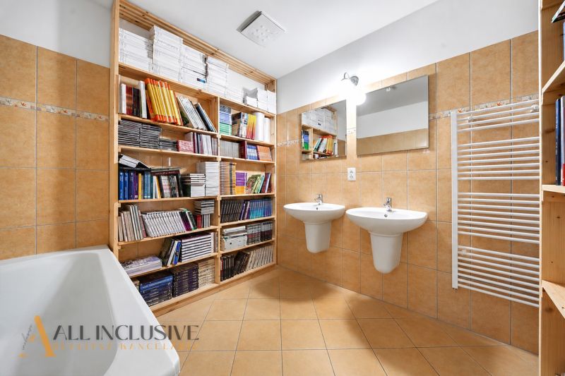 A bathroom in a 3-room apartment with books, two sinks, and tiles.
