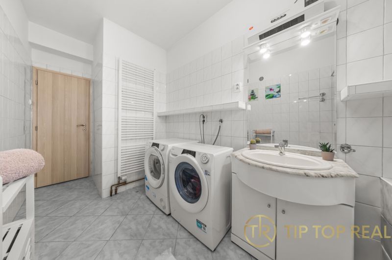 Washing machine and dryer in the bathroom of a family house with white tiles and a mirror.